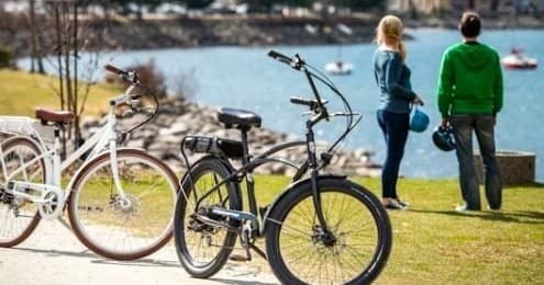 Couple beside parked e-bikes on waterfront trail, scenic park