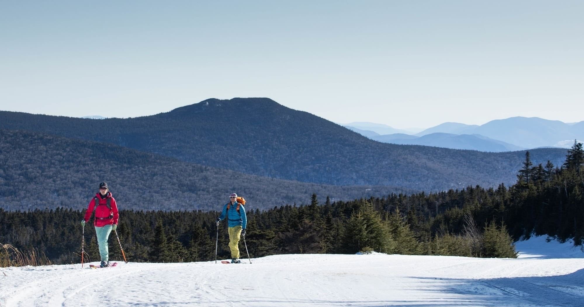 Skiers traversing open snowy ridge with distant mountain views