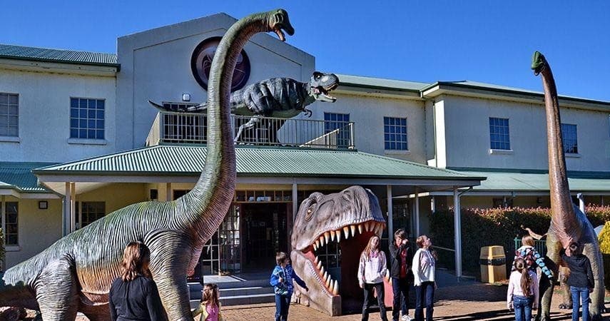 Families exploring outdoor dinosaur exhibit in front of museum entrance