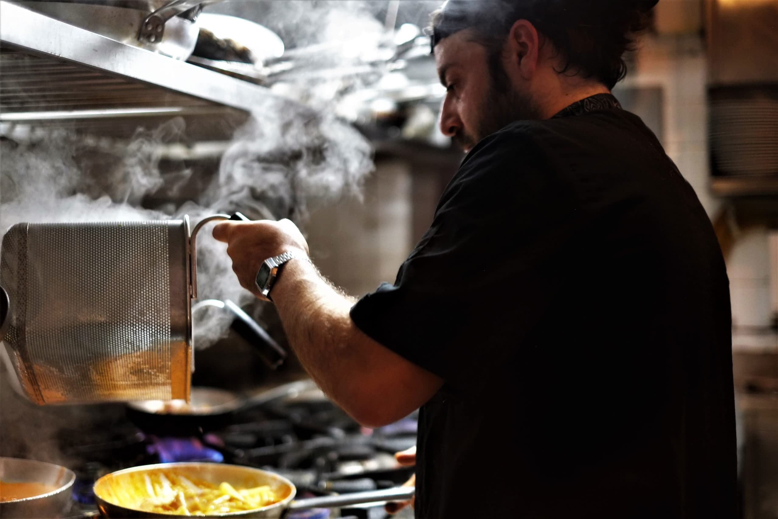 Chef cooking pasta with steaming pans in professional kitchen
