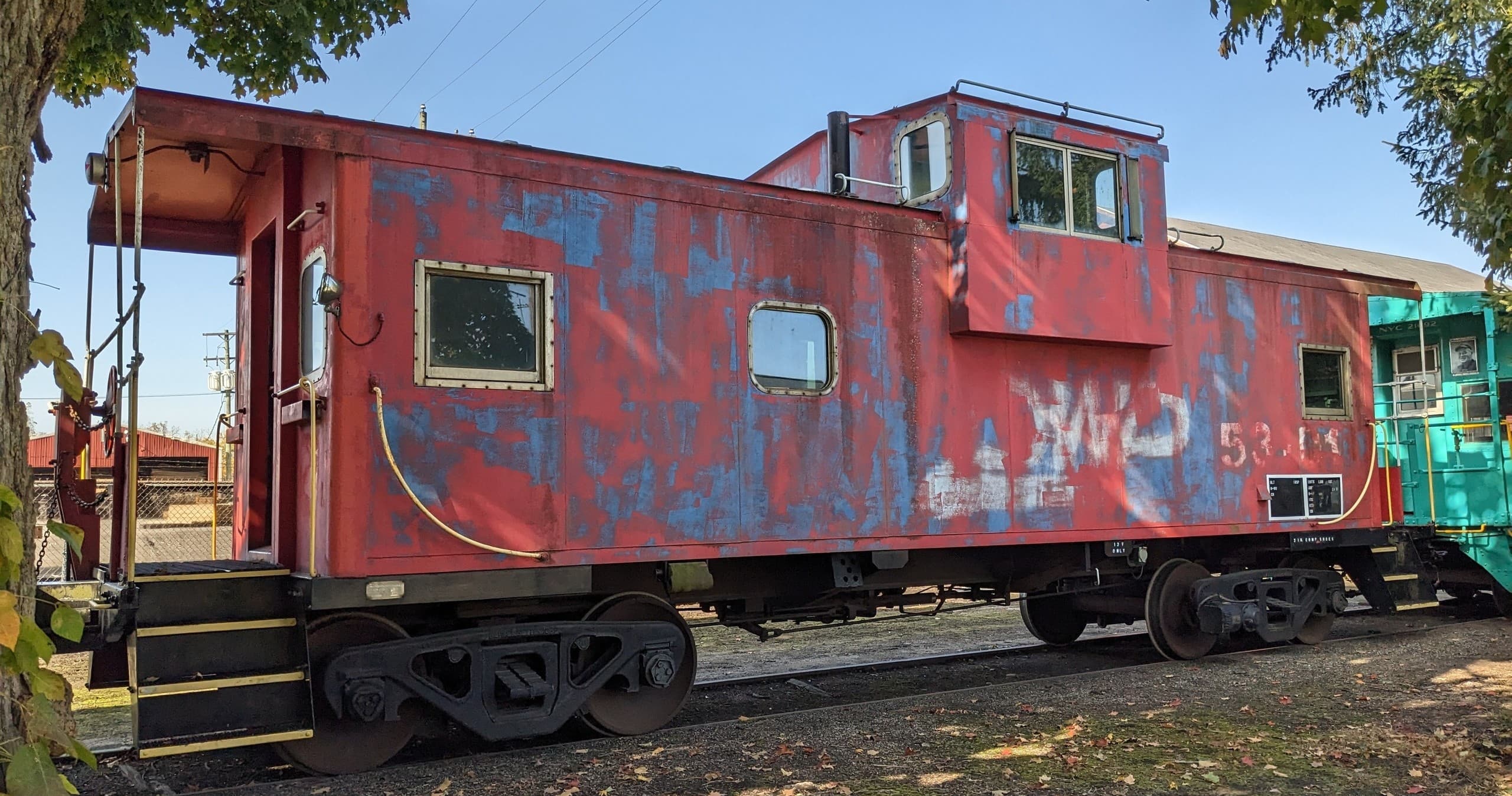 Weathered red caboose parked by trees on grassy rail siding