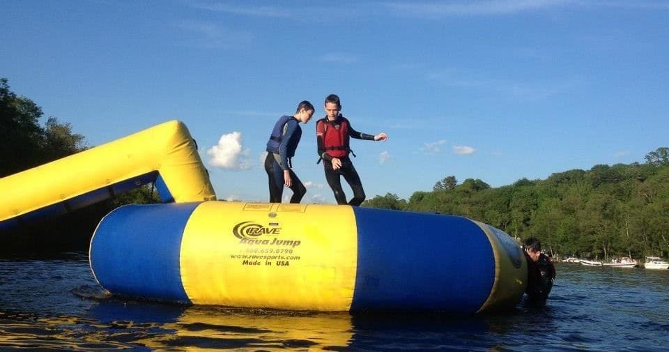 Children jumping on inflatable water blob at castle lake