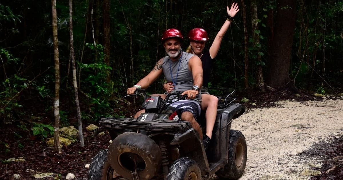 Couple riding ATV on muddy rainforest path during excursion