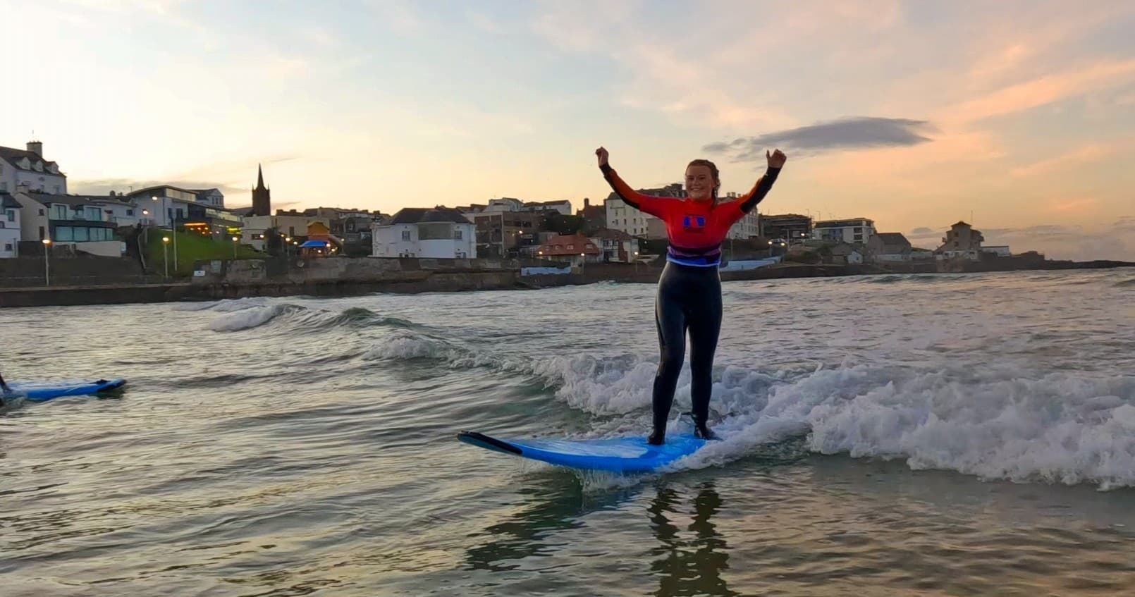 Surfer standing on board catching small wave at sunset beach