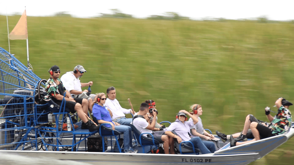 Passengers on airboat cruising swiftly past tall marsh grasses