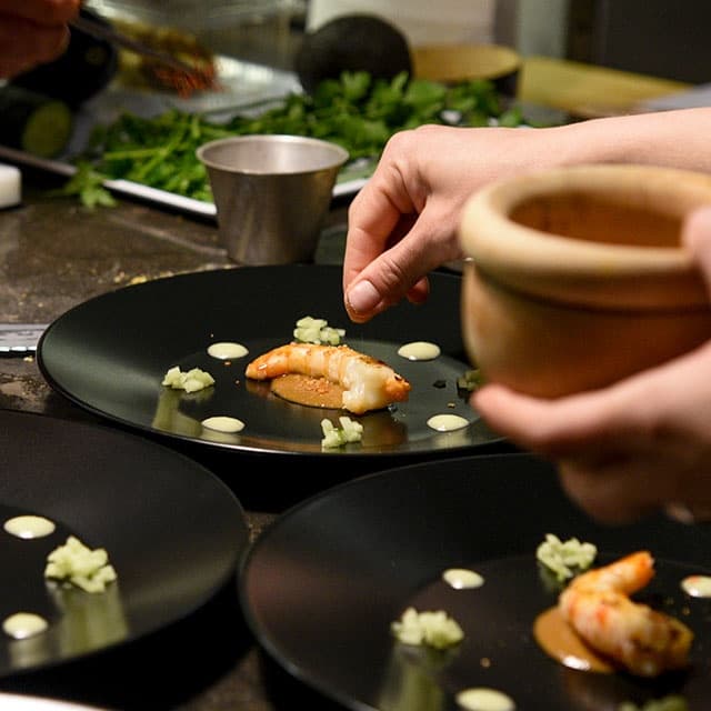 Chef plating gourmet shrimp on black plates in professional kitchen