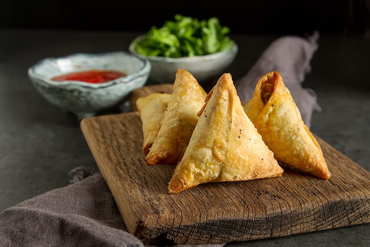 Crispy vegan samosas on wooden board with dipping sauce, tabletop