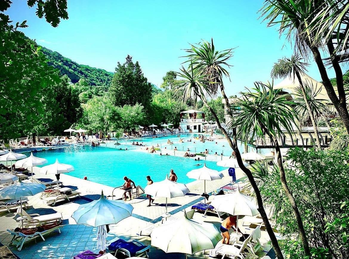 Outdoor thermal resort pool with palm trees and sun umbrellas
