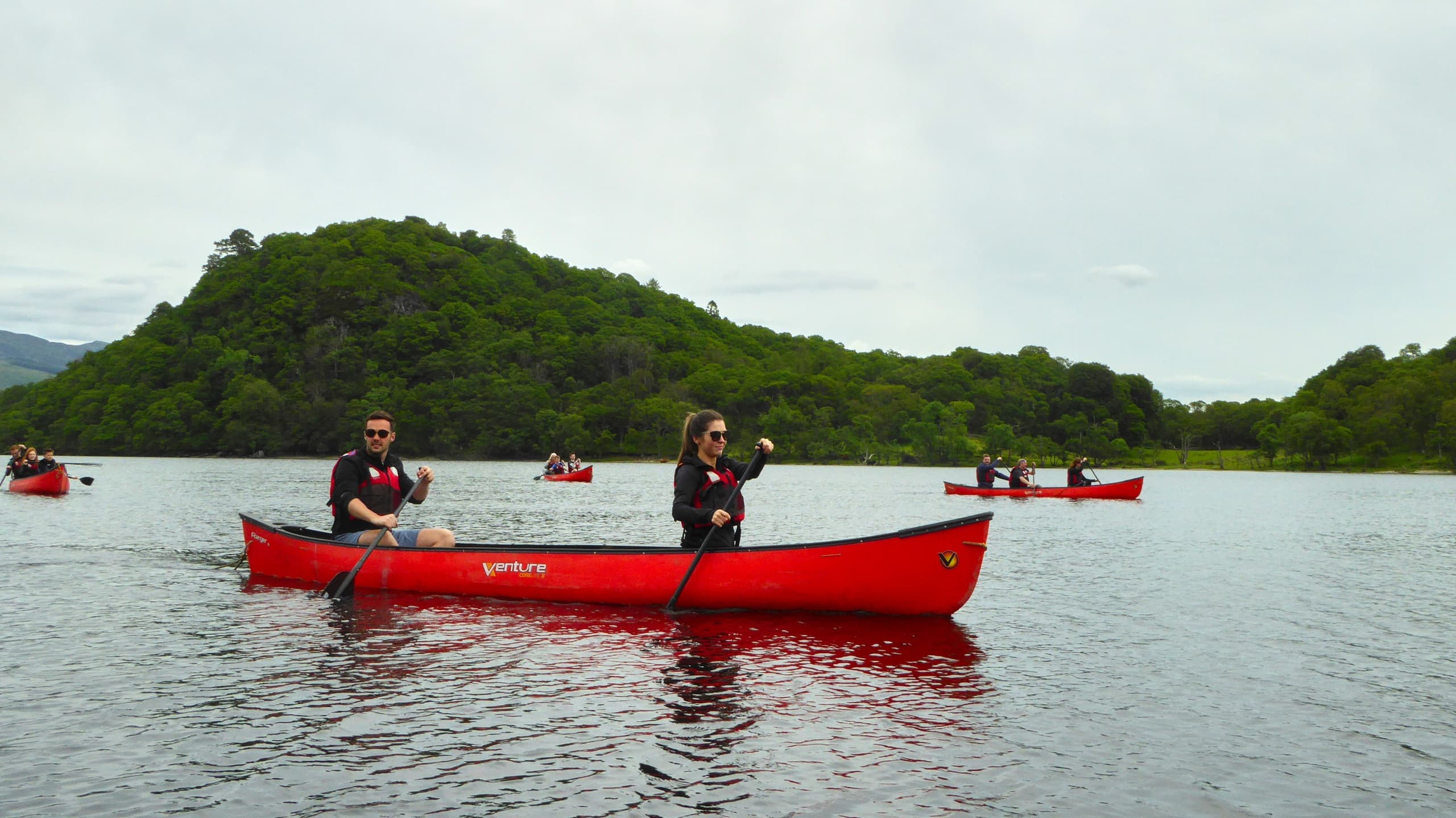 Two people canoeing on Loch Lomond near wooded island