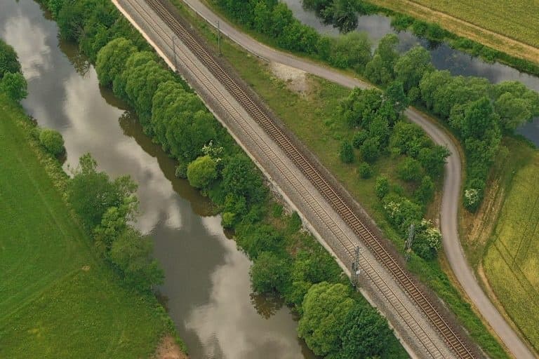 Aerial sweep of river bend with tracks and green fields, paddling route