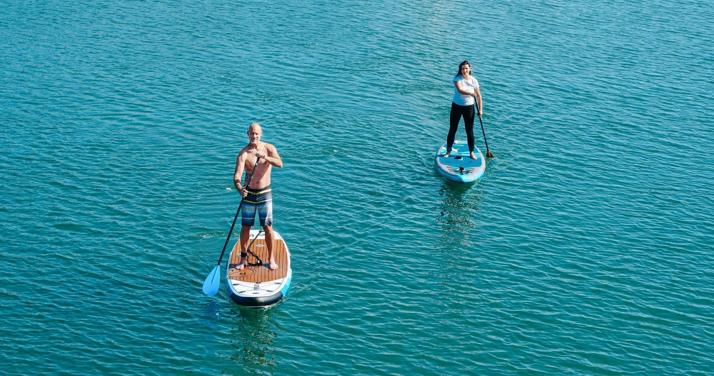 Aerial stand-up paddleboarding over clear turquoise coastal water