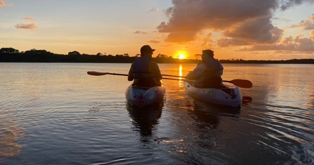 Couple kayaking at sunset with reflective open-water vista
