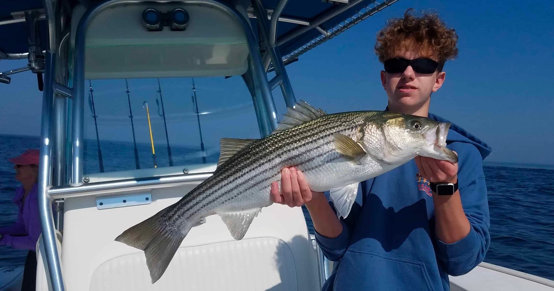 Angler holding striped bass aboard center-console boat, offshore