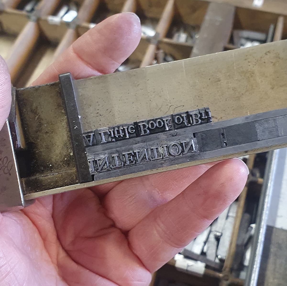Hand holding metal letterpress type in printshop, composing text blocks