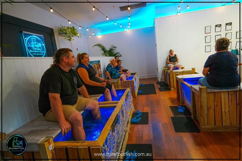 Group of customers enjoying fish pedicure in illuminated clinic