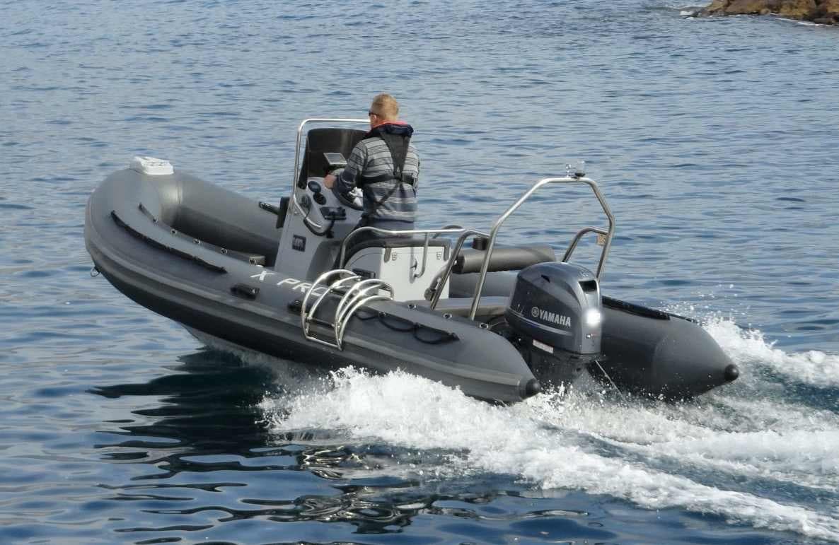Gray RIB tender cruising near rocky coast with operator at helm