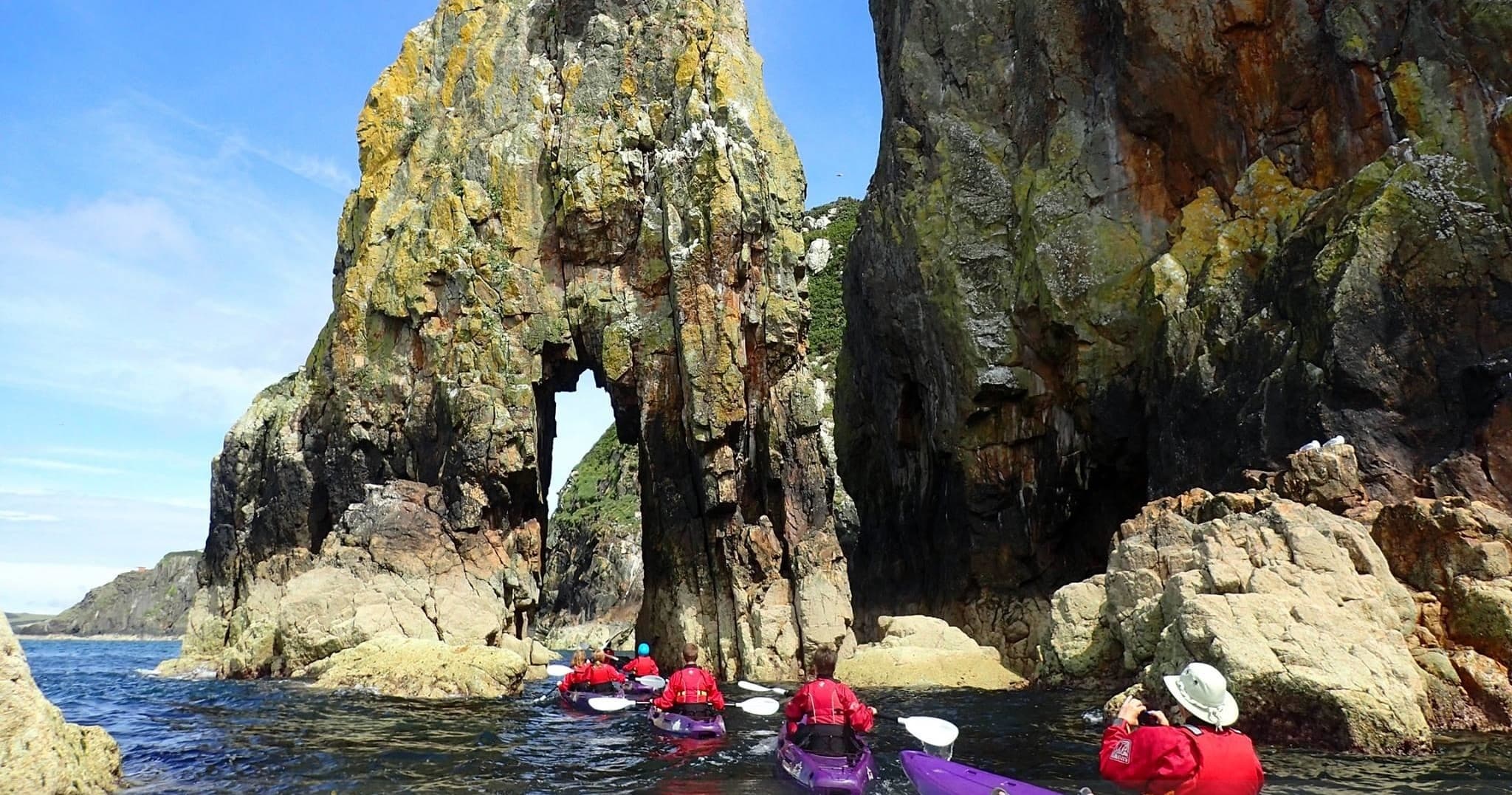 Kayakers paddling through coastal rock arch on sunny day