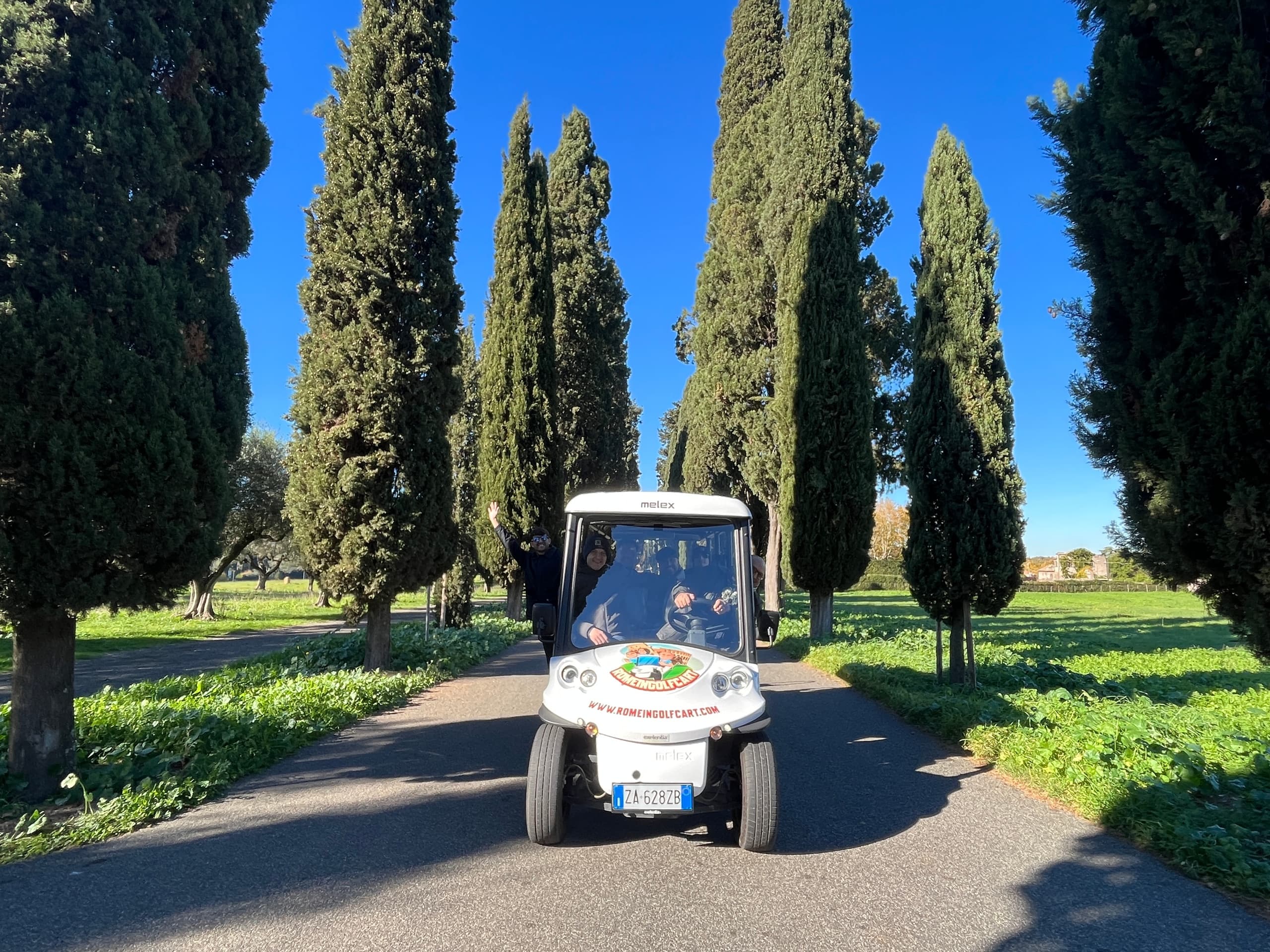 Golf cart cruising cypress-lined road near Rome villas