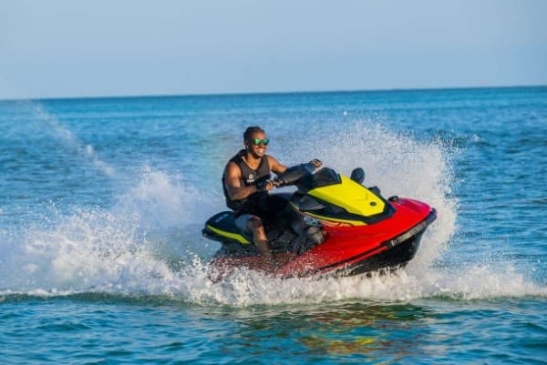 Man jet skiing on clear coastal waters, splashing through waves