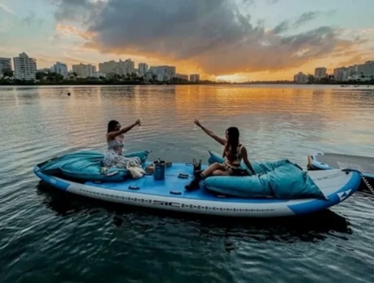 Couple paddling on inflatable raft at sunset over lagoon