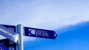 Trail and peak signpost against blue sky pointing to mountain summit
