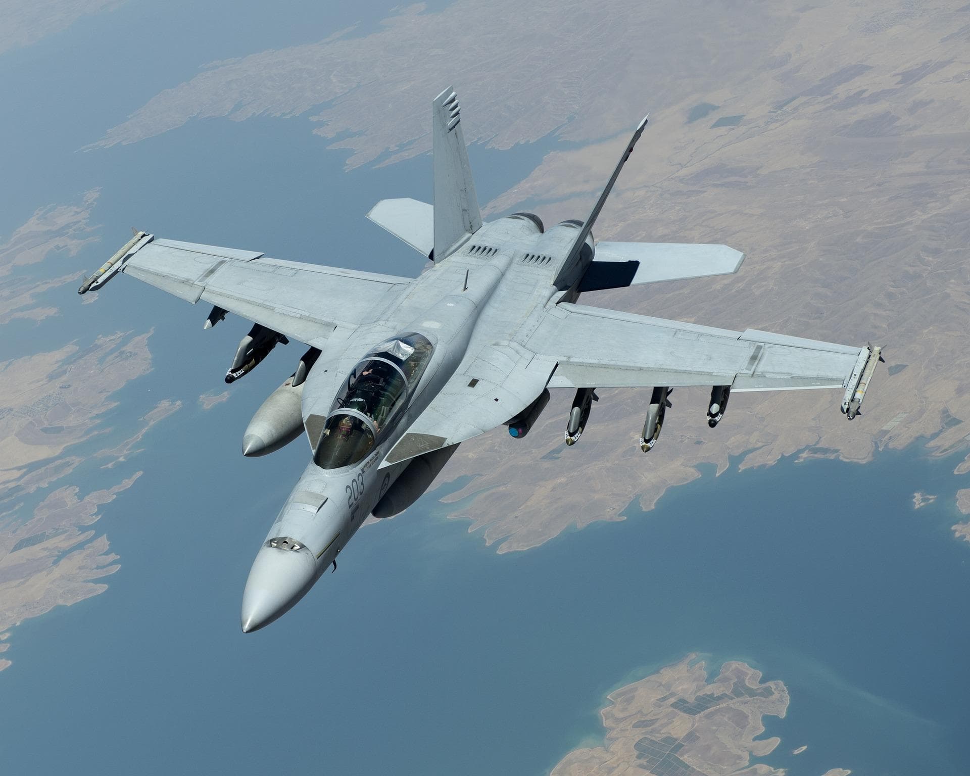 Single fighter jet flying over desert coastline, dynamic aerial shot