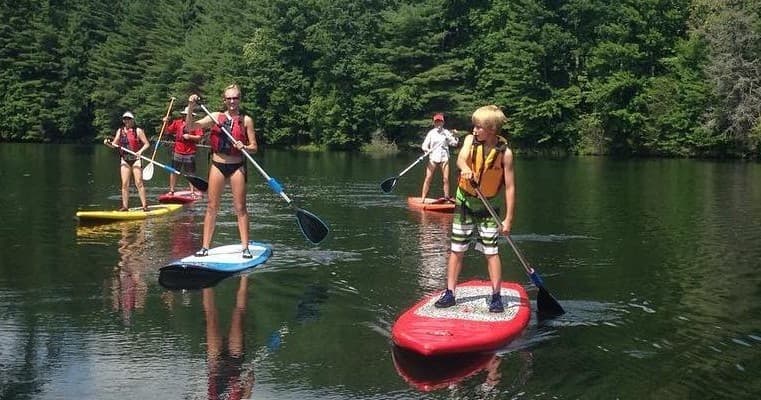 Group stand-up paddleboarding on a calm lake framed by trees