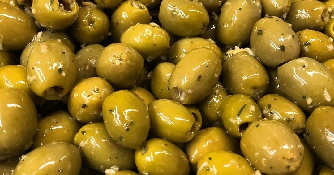 Marinated green olives glistening in oil at deli salad bar