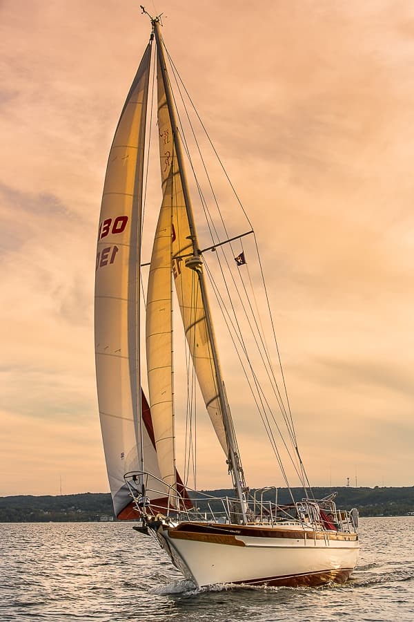 Tall sailboat gliding at golden sunset, scenic coastal sail