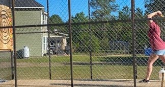 Axe thrower outdoors at fenced range practicing throws