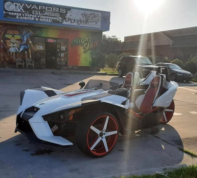 White Polaris Slingshot parked outside OBX shop at sunset