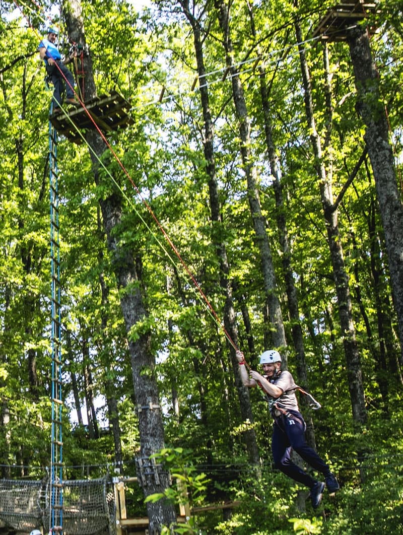 Participant zipping across high zipline through dense forest canopy