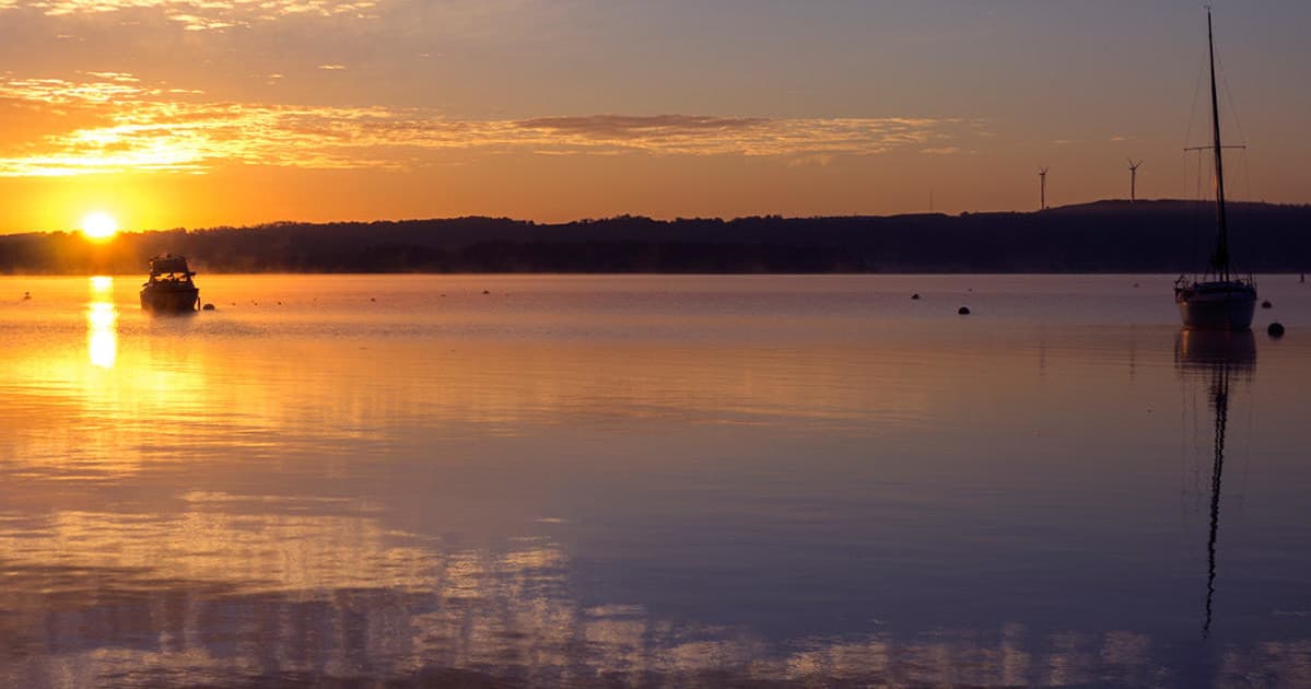 Sunset over calm lake with anchored boats and reflections