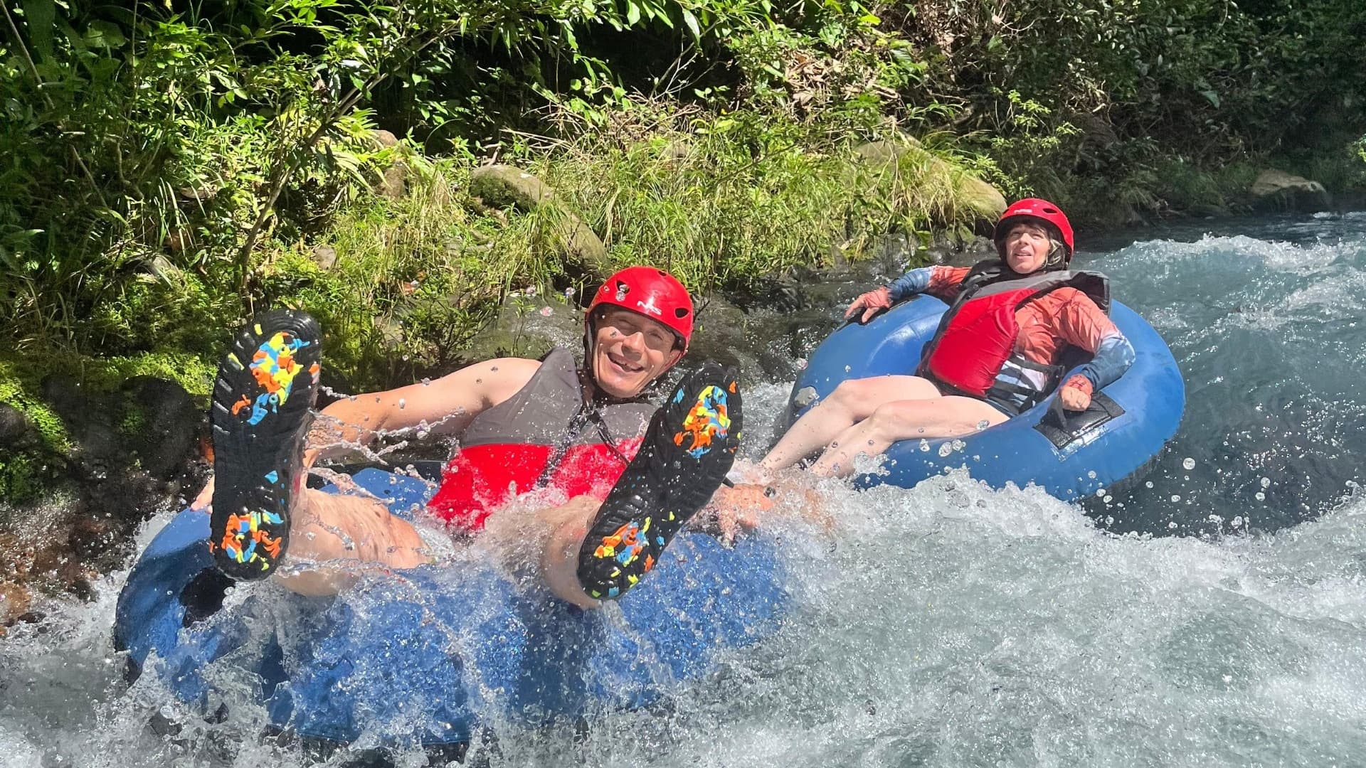 Two tubers navigating whitewater on a lush tropical river