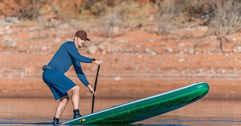 Man paddleboarding on calm lake near red sandstone shoreline