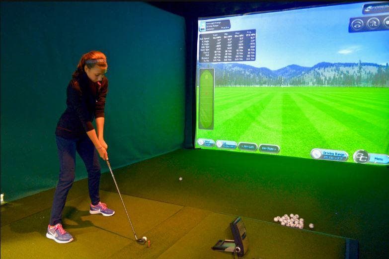 Golfer practicing swing in indoor simulator bay with screen