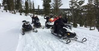 Snowmobiles racing on groomed forest trail through deep snow