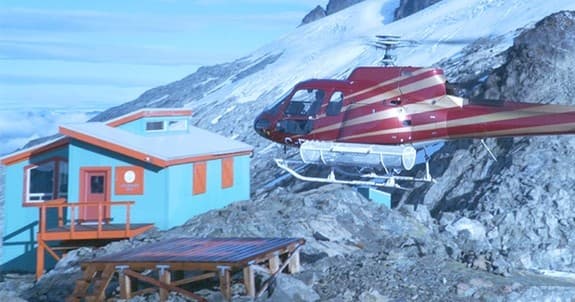 Helicopter landing near alpine shelter on rocky glacier moraine