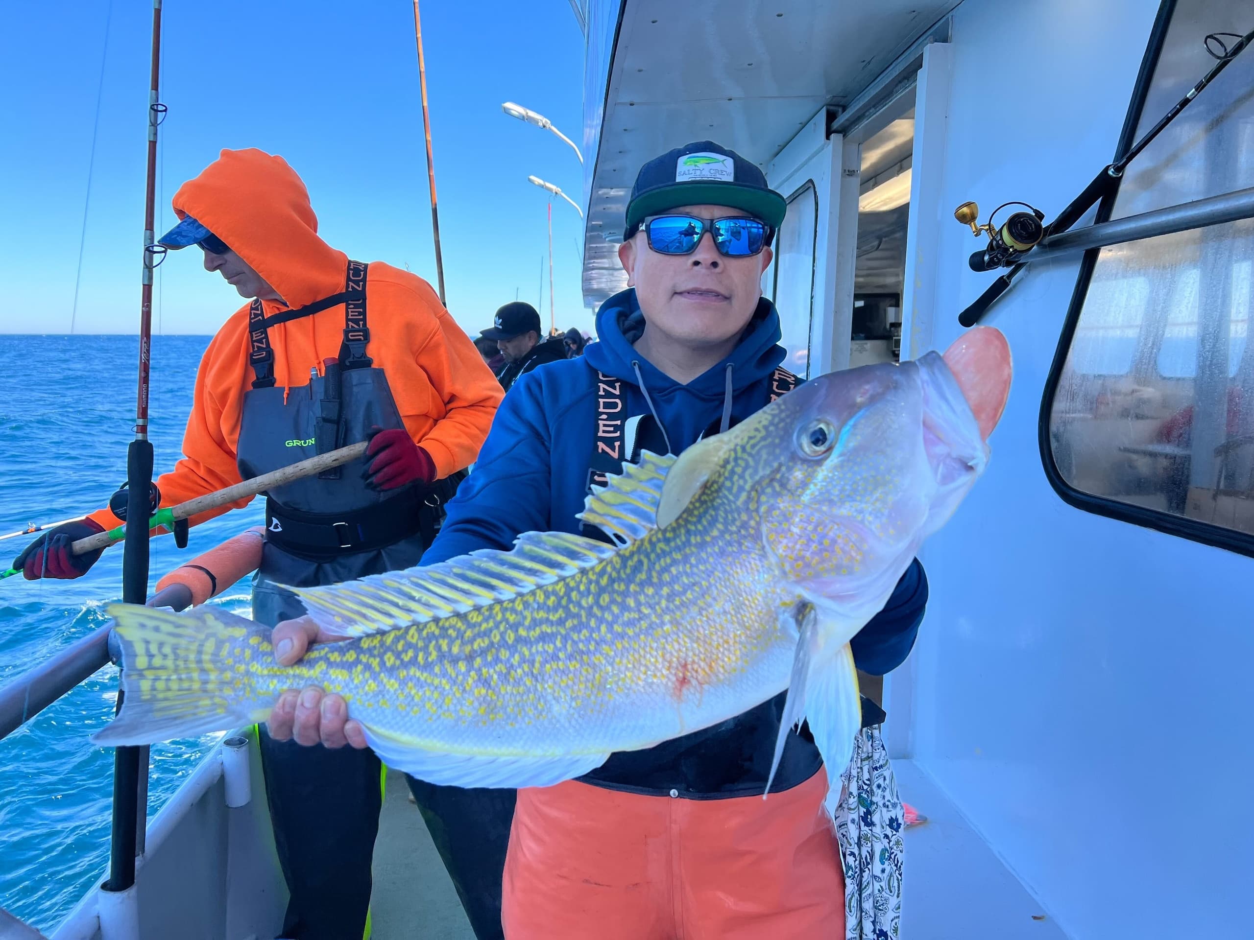 Angler holding large cod aboard fishing charter with ocean backdrop