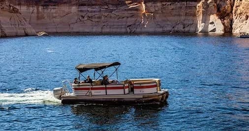 Pontoon boat cruising blue waters of Lake Powell near cliffs