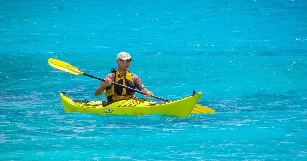 Solo paddler in bright yellow kayak on tropical turquoise sea