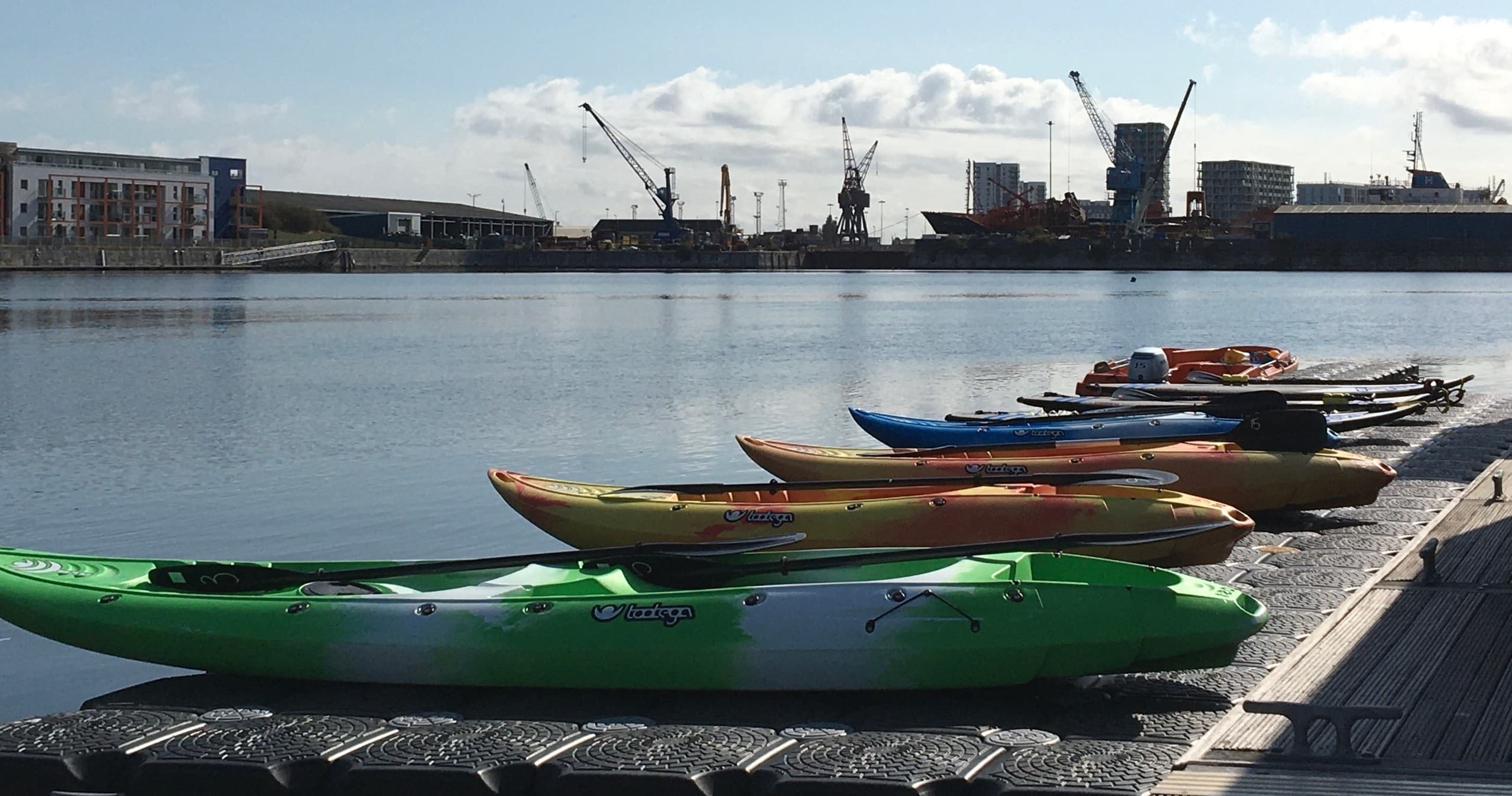 Colorful kayaks lined on dock at marina with industrial harbor backdrop
