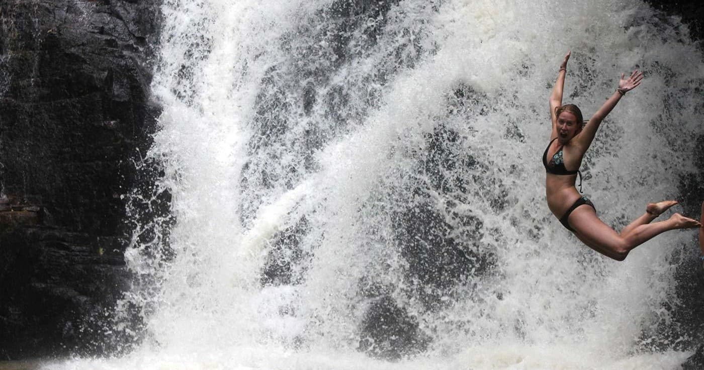Adventurer jumping from rock into powerful cascading waterfall