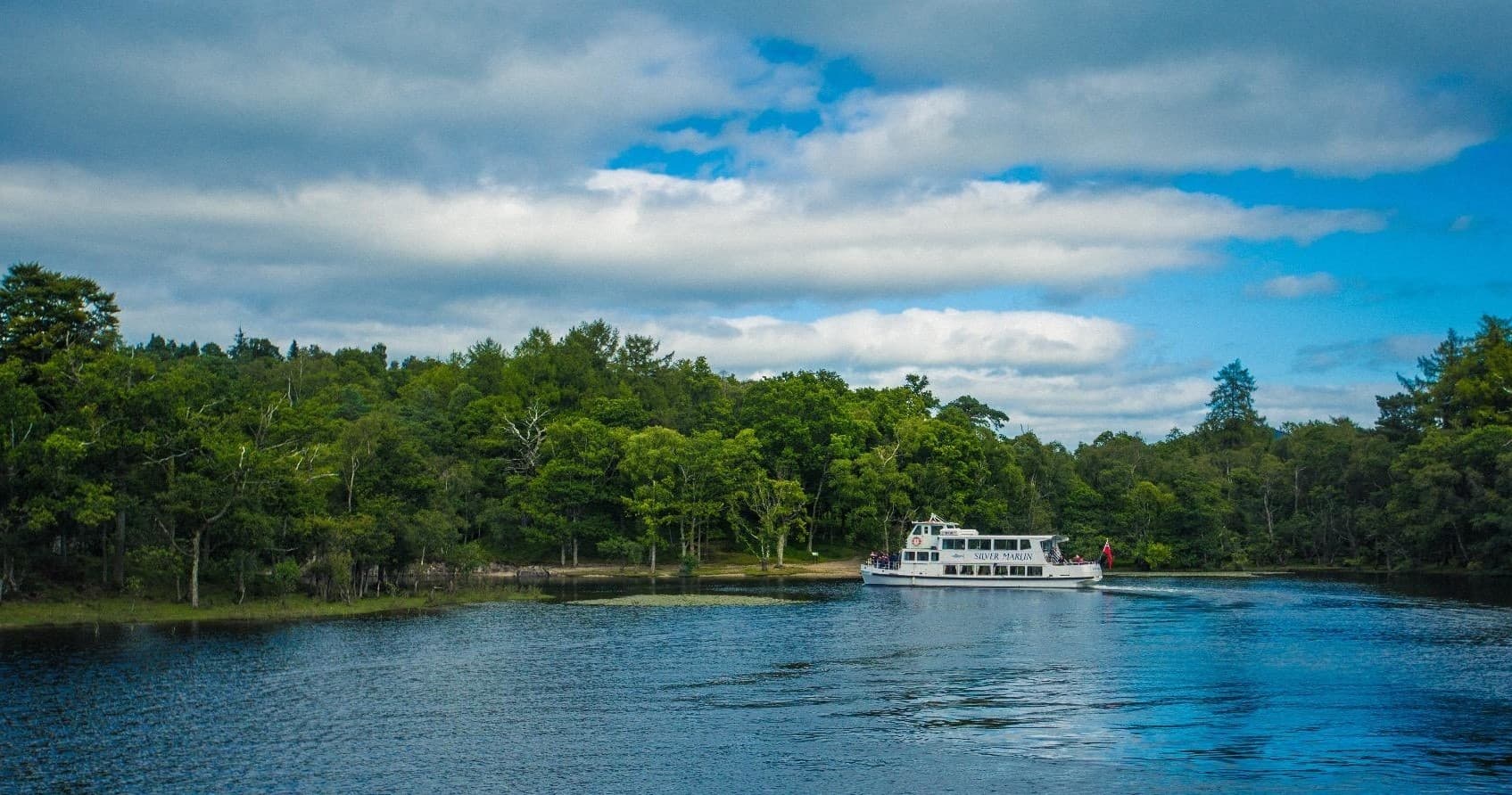 Tour boat cruising near forested shoreline on clear lake