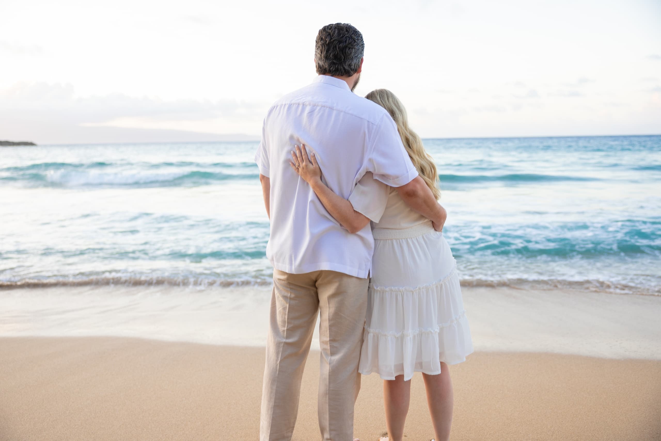 Couple embracing on sandy beach at ocean shoreline at sunset
