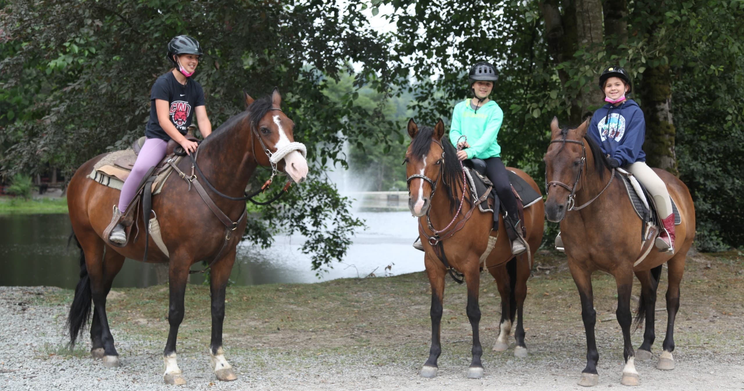 Three riders on horses by lakeshore ready for trail ride