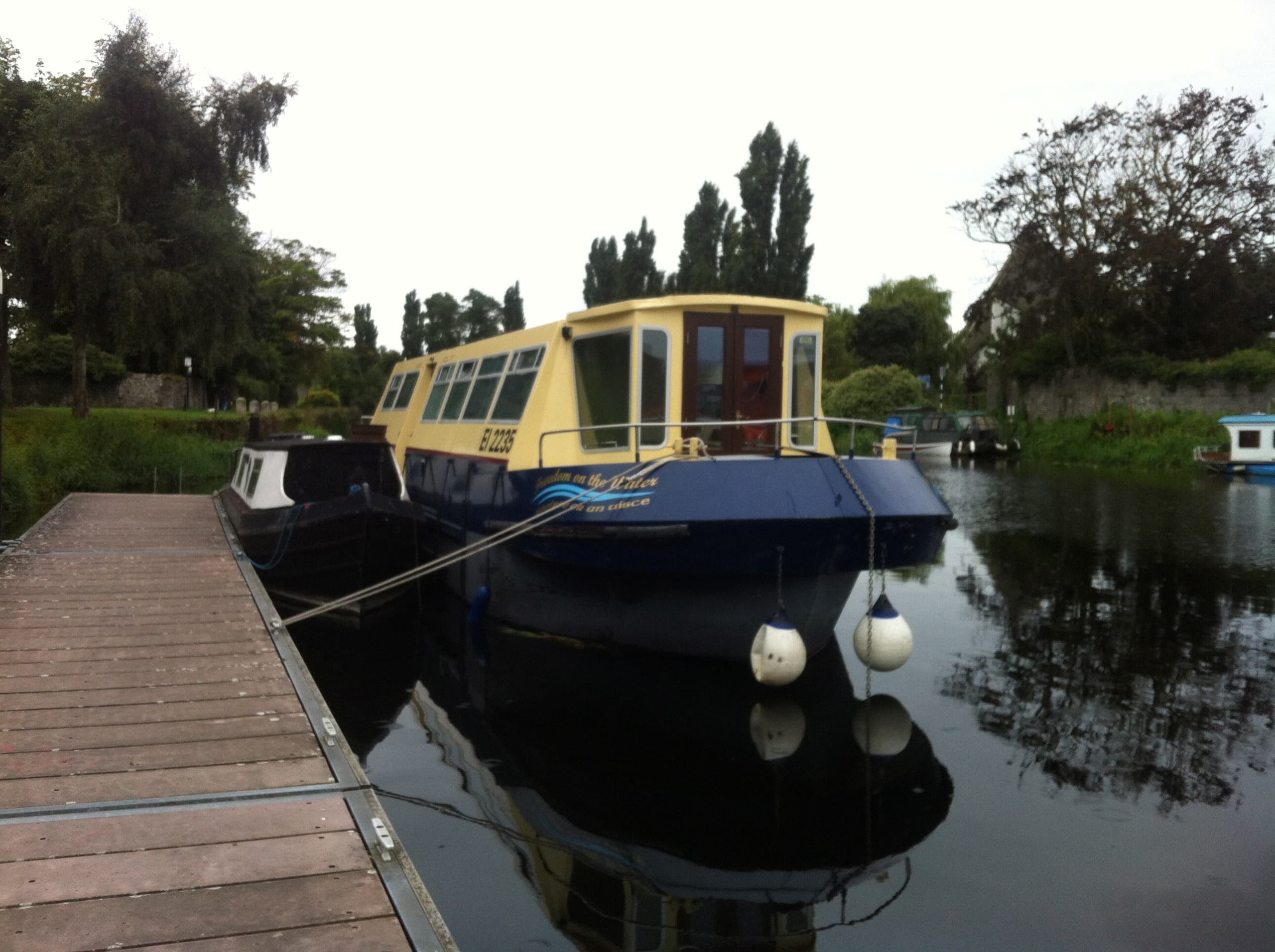 Small passenger boat moored at wooden dock with calm reflections