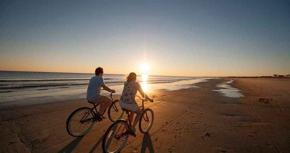 Couple bicycling on sunset beach shoreline at Hilton Head