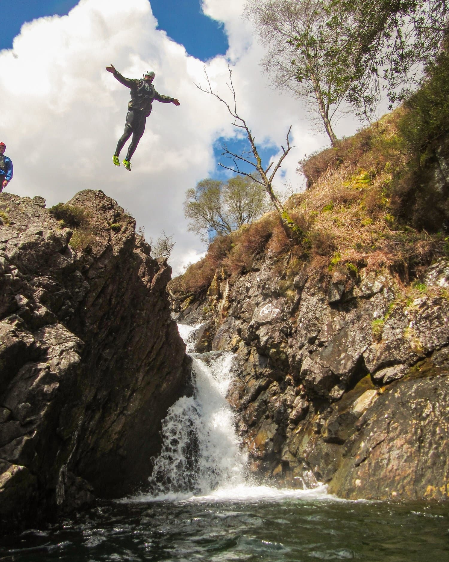Cliff jumper leaping into alpine pool below waterfall canyon