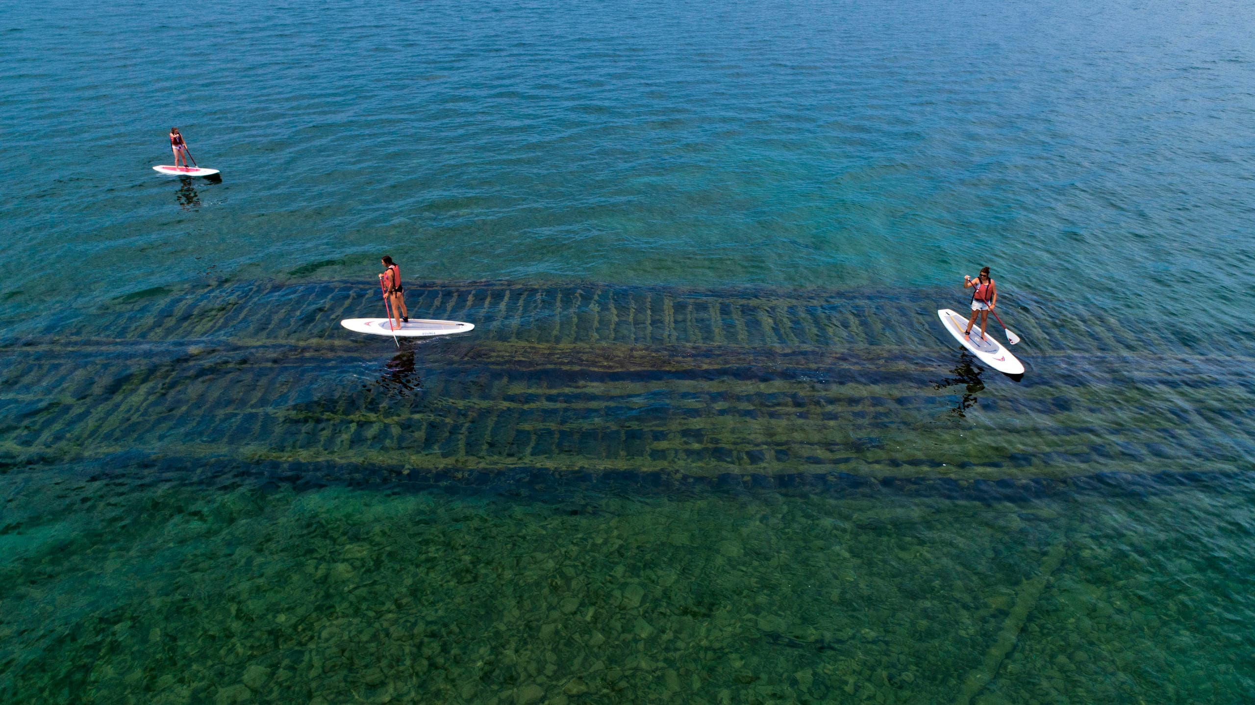 Aerial paddleboarders cruising over shallow clear coastal waters